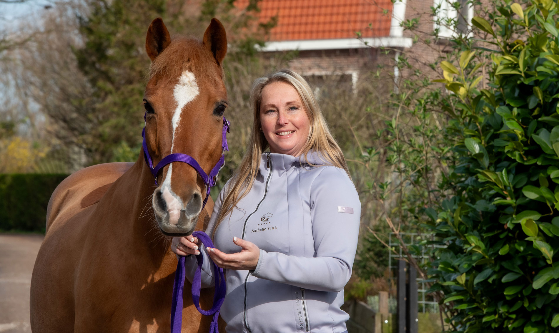nathalie vink houdt een van haar therapiepaarden vast en kijkt in de camera