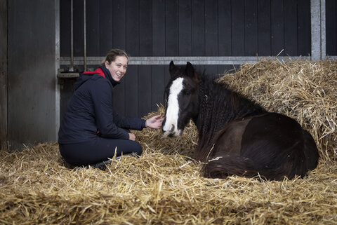 kim zit naast een paard dat op het stro ligt