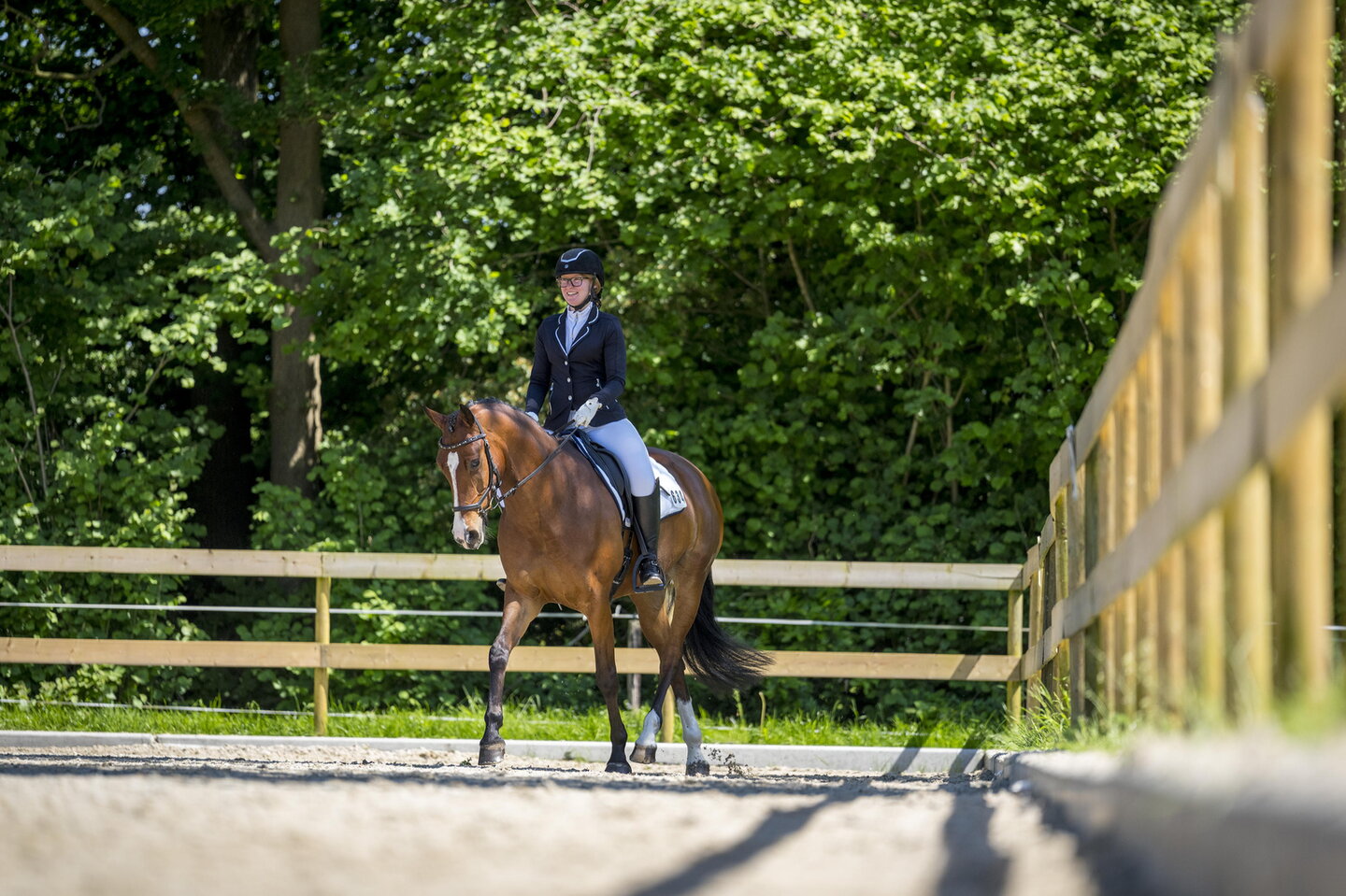 Moniek de Lange rijdt op een bruin paard in de rijbak in wedstrijdoutfit
