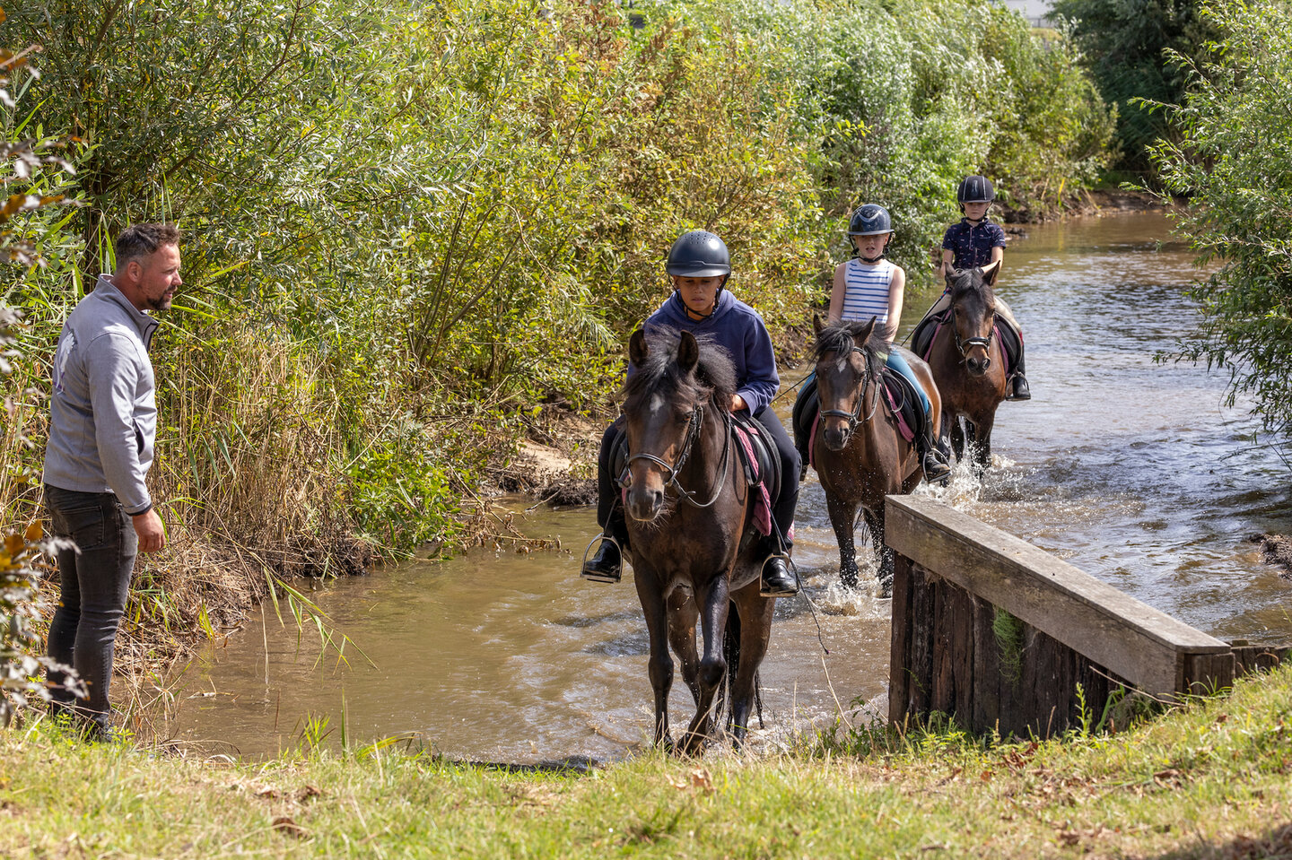 yorick baecke begeleidt de kinderen terwijl ze met pony door het water gaan